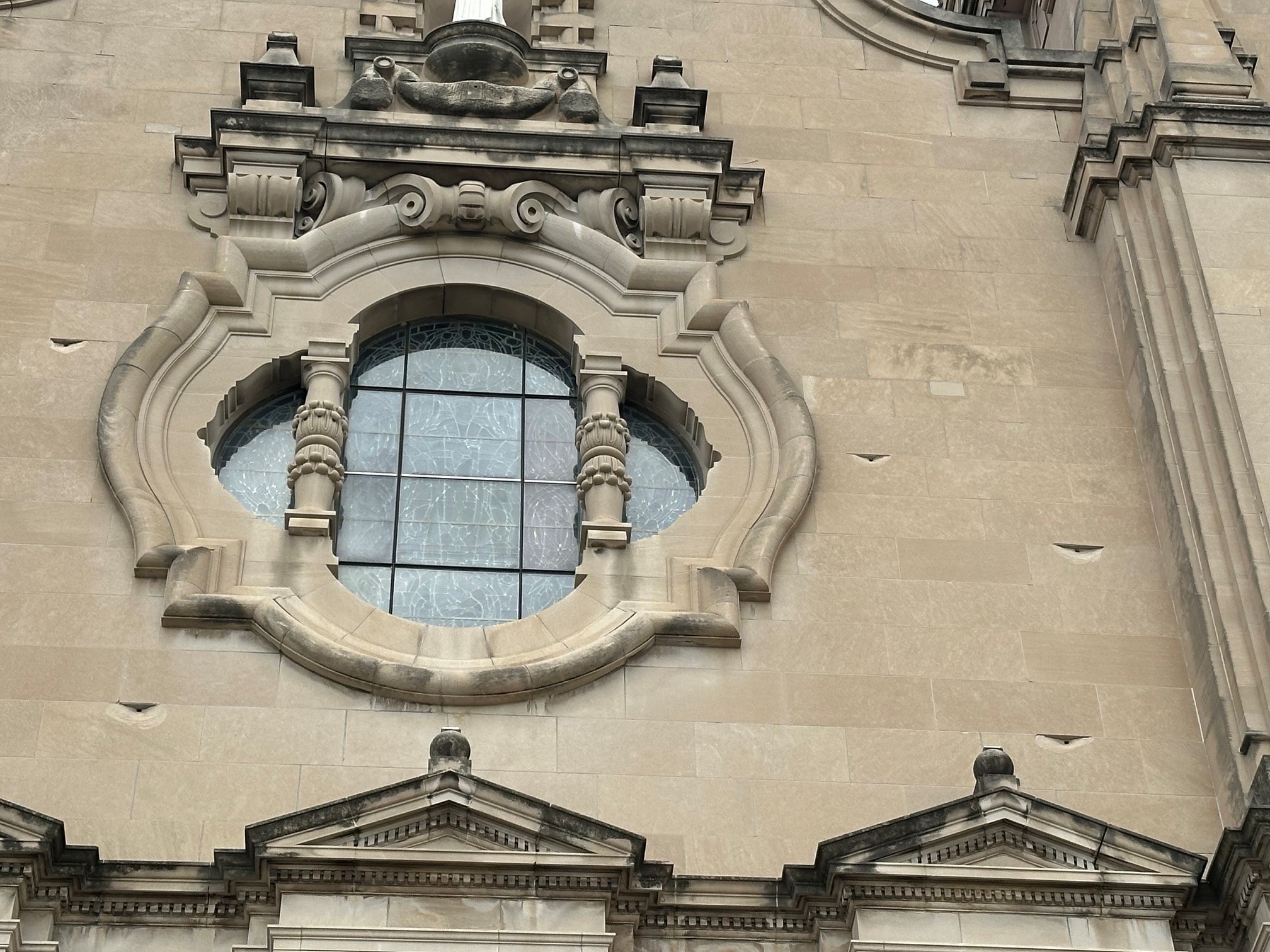 West facade spalling - St. Cecilia Cathedral Ornate stone building facade with a circular arched window and decorative molding above the window feature.